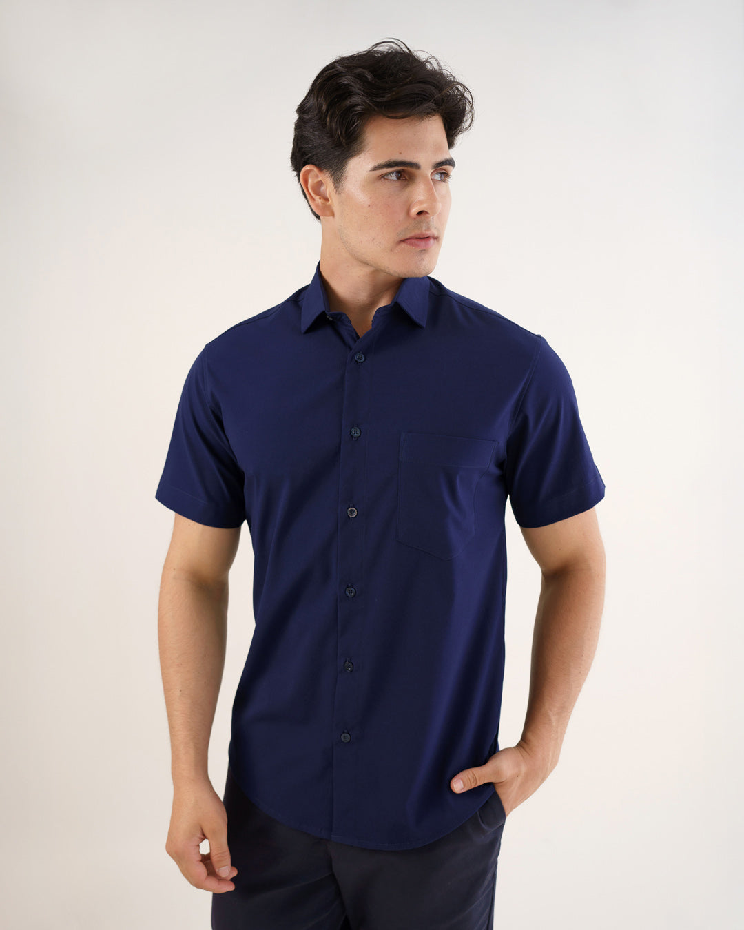 Camisa social masculina manga curta azul marinho em vista frontal, com mao no bolso da calca e botoes fechados — foto 5