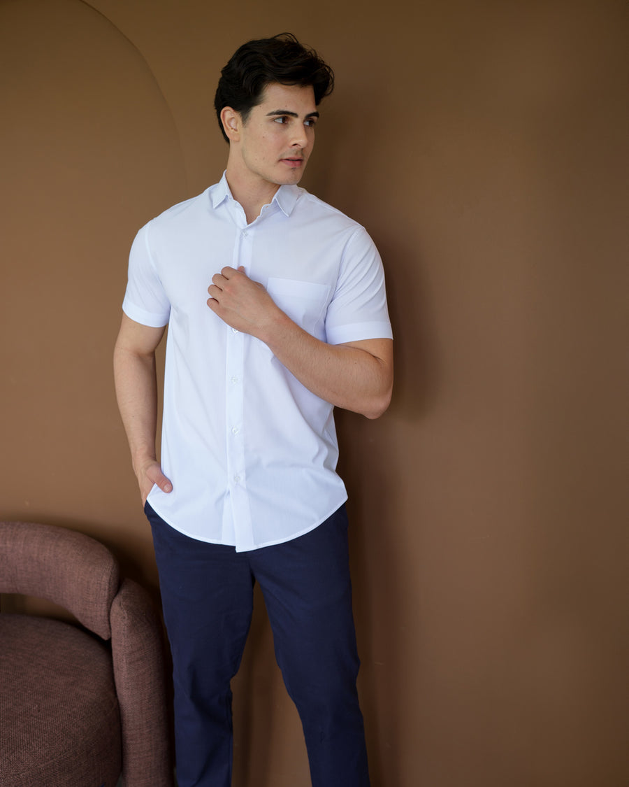 Camisa social masculina manga curta branca em vista frontal, modelo ajustando a gola com bolso visivel