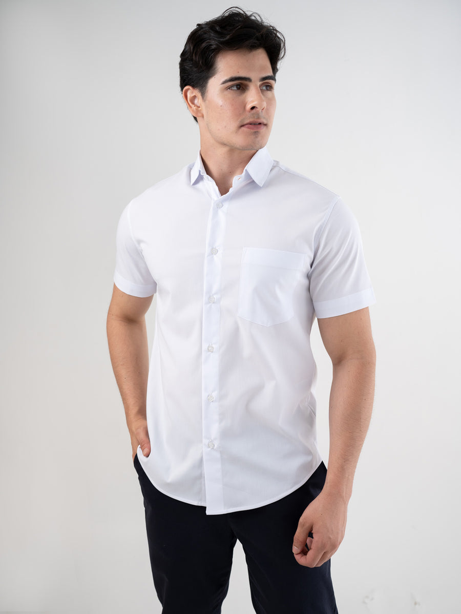 Camisa social masculina manga curta branca em meio corpo frontal, com mao no bolso da calca e gola aberta
