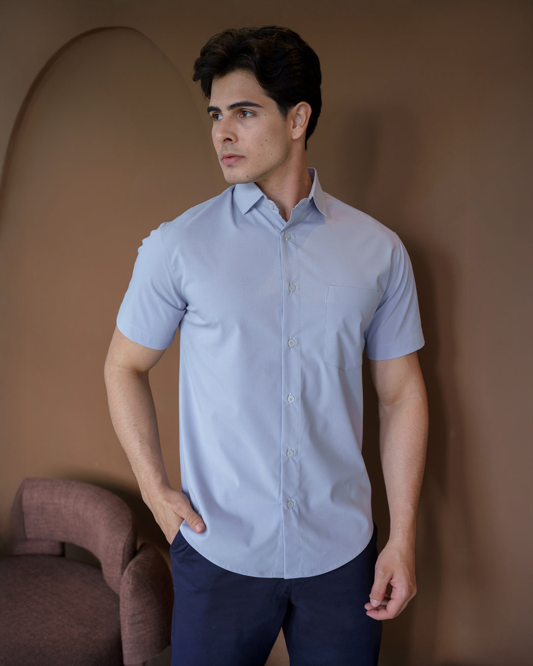 Camisa social masculina manga curta cinza claro em meio corpo frontal, com mao no bolso da calca e gola aberta — foto 2