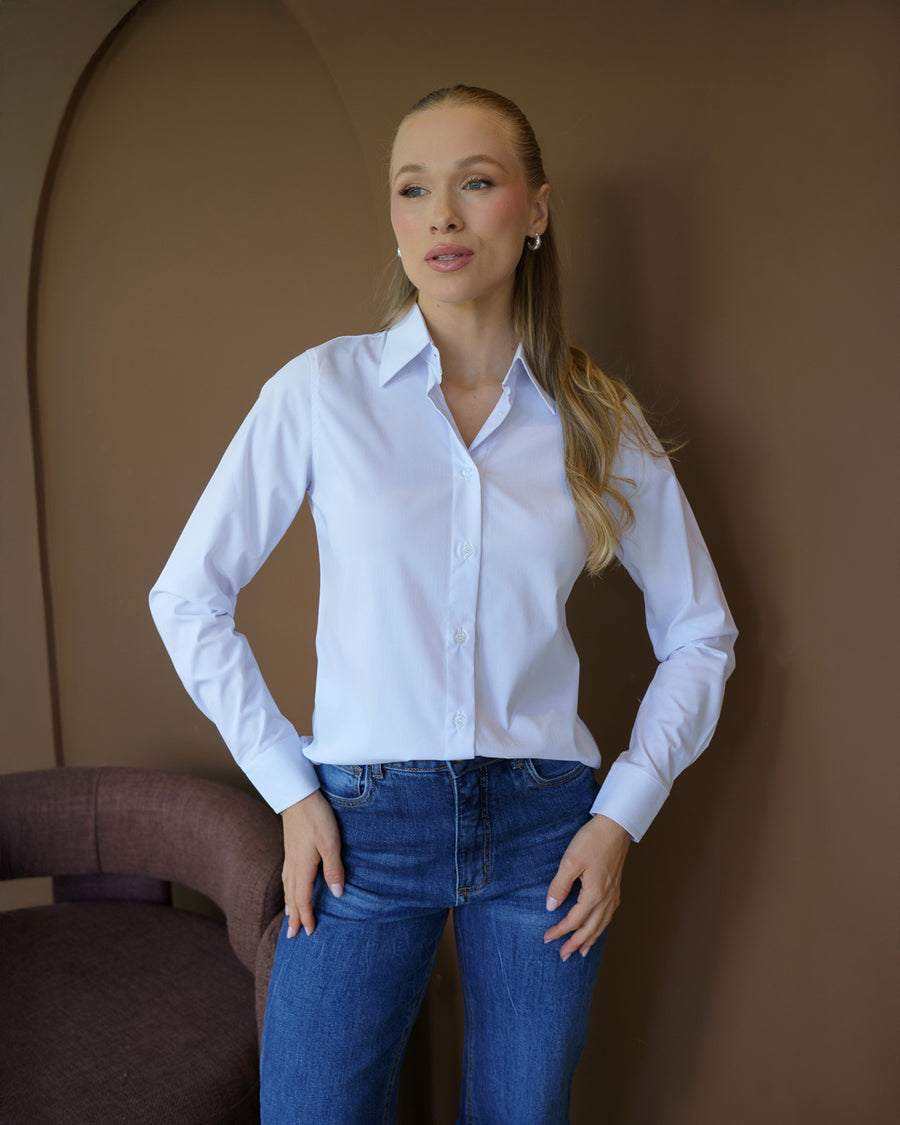 Camisa social feminina manga longa branca em meio corpo frontal, com maos na cintura mostrando punhos longos
