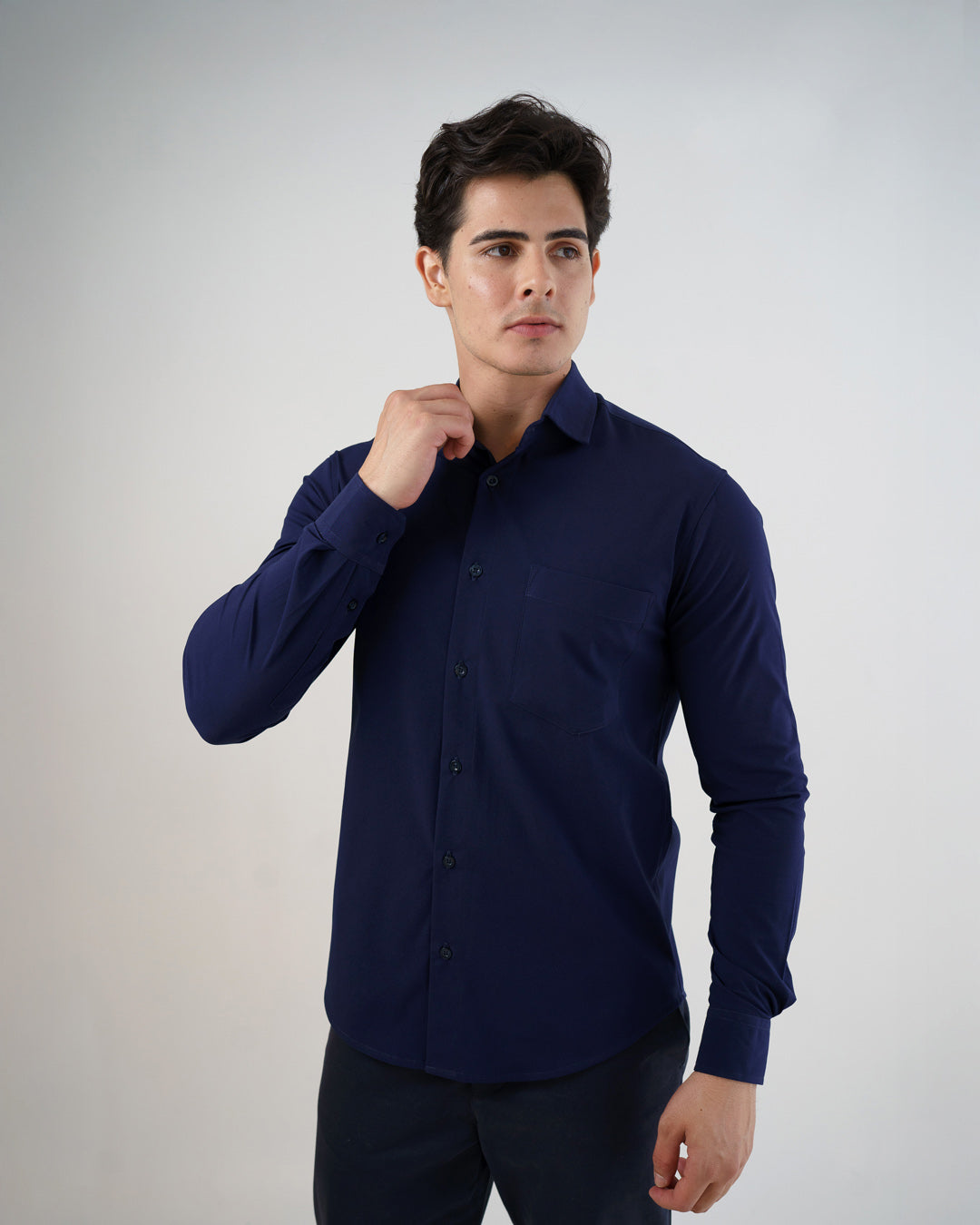 Camisa social masculina manga longa azul marinho em vista frontal, modelo ajustando a gola com bolso visivel — foto 4