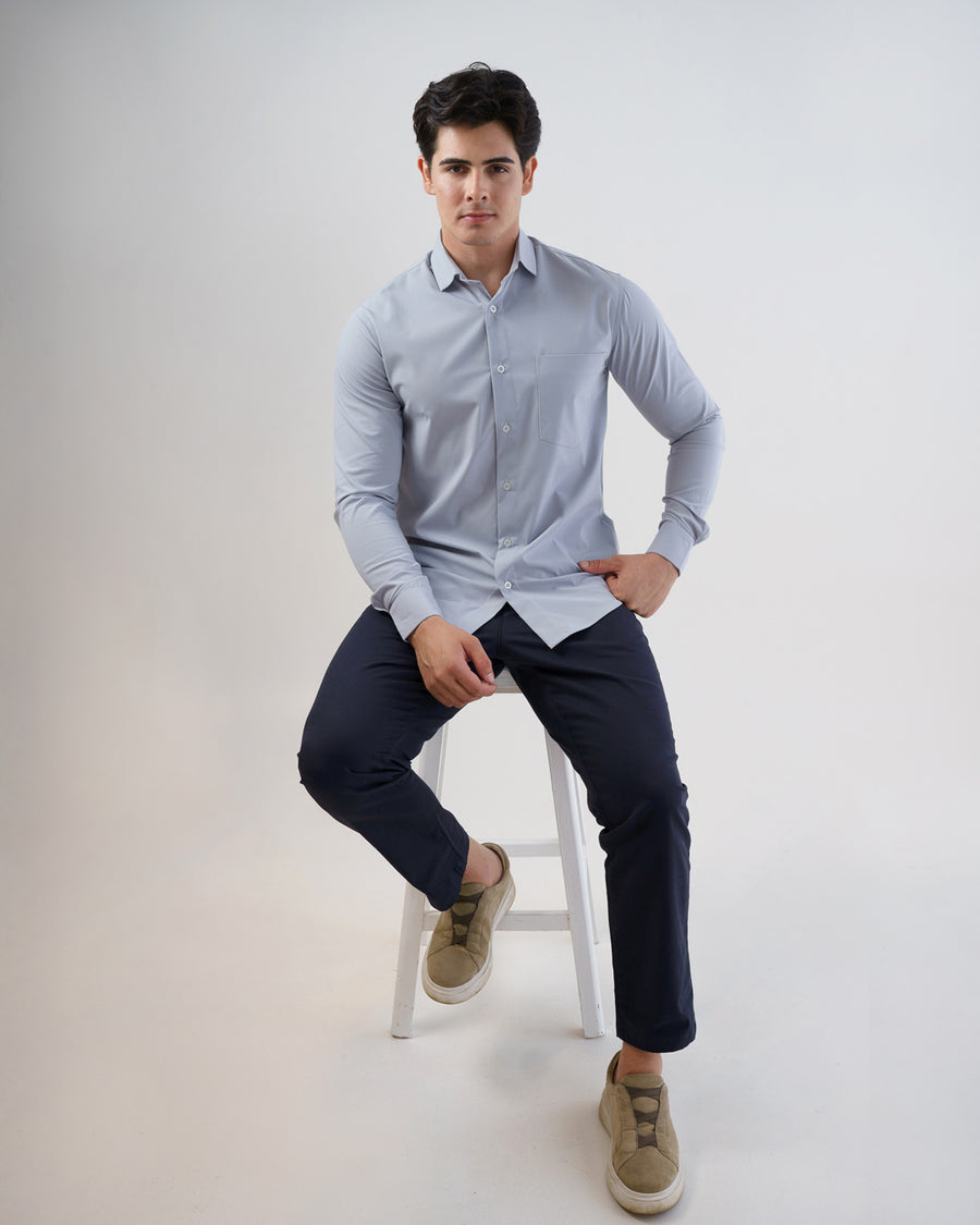 Camisa social masculina cinza claro, modelo sentado em banquinho mostrando o caimento slim da peça