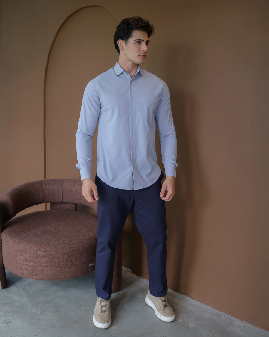 Camisa social masculina cinza claro em corpo inteiro, modelo veste a camisa com calça azul marinho