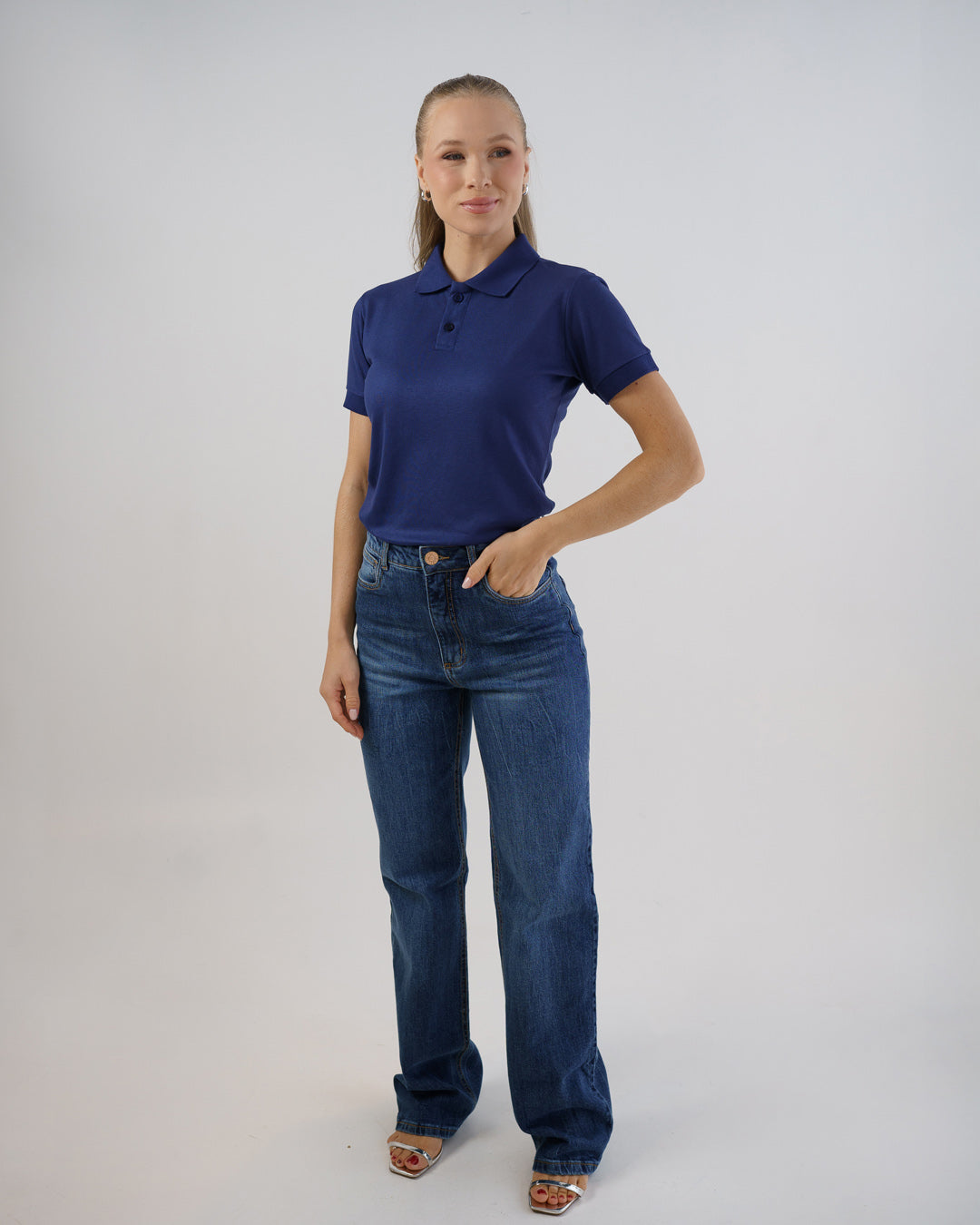 Camiseta polo feminina azul marinho em corpo inteiro, modelo veste a polo com calça jeans clara — foto 2