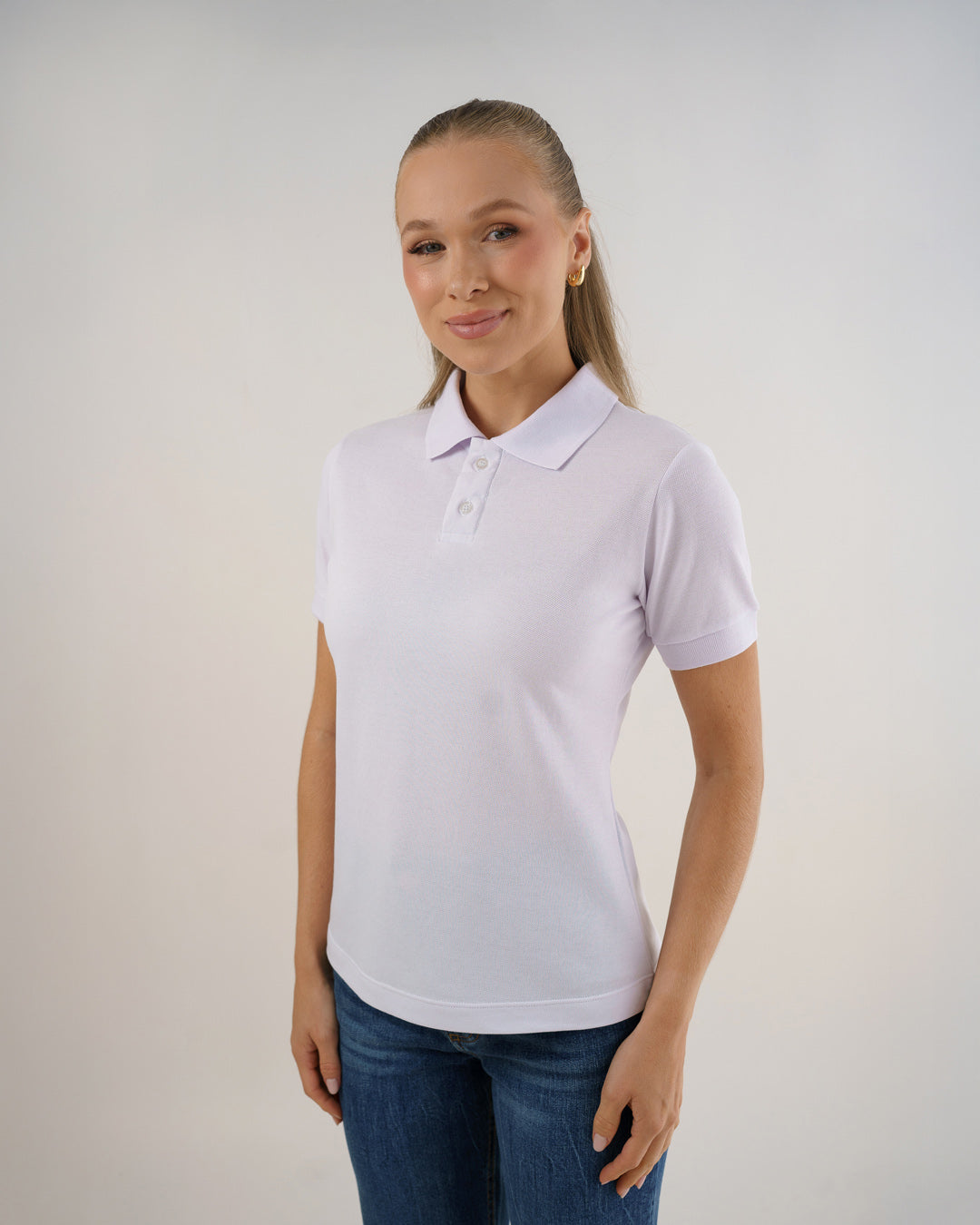 Camiseta polo feminina premium branca em meio corpo de leve perfil, com gola, dois botões e jeans
