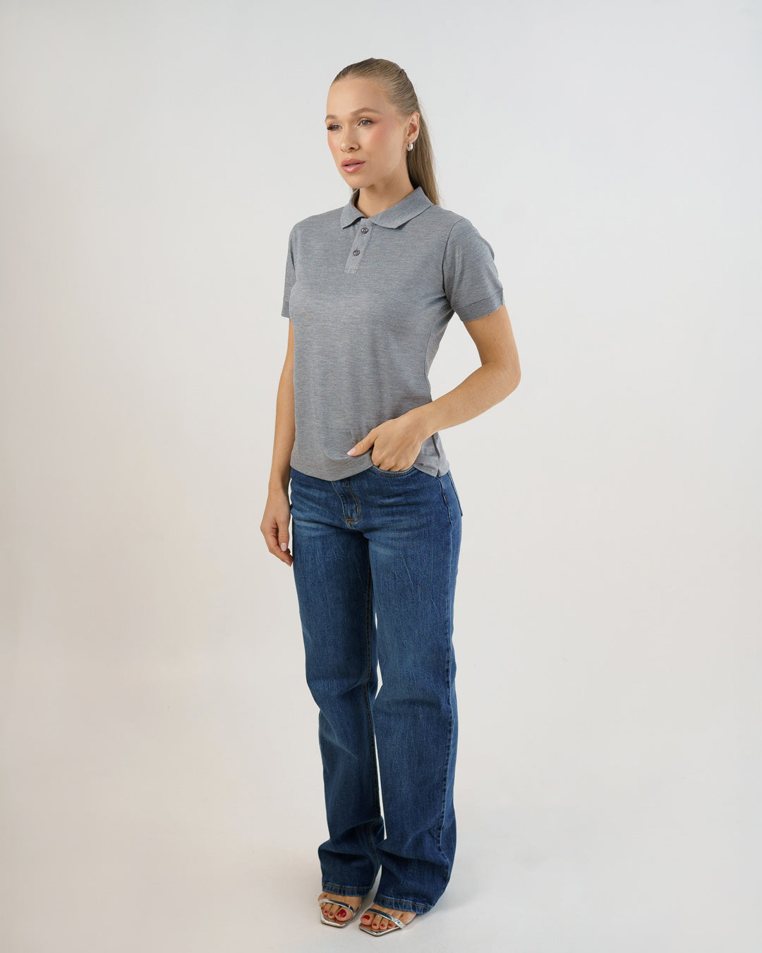 Camiseta polo feminina cinza claro em corpo inteiro de leve perfil, modelo com mão no bolso do jeans — foto 2