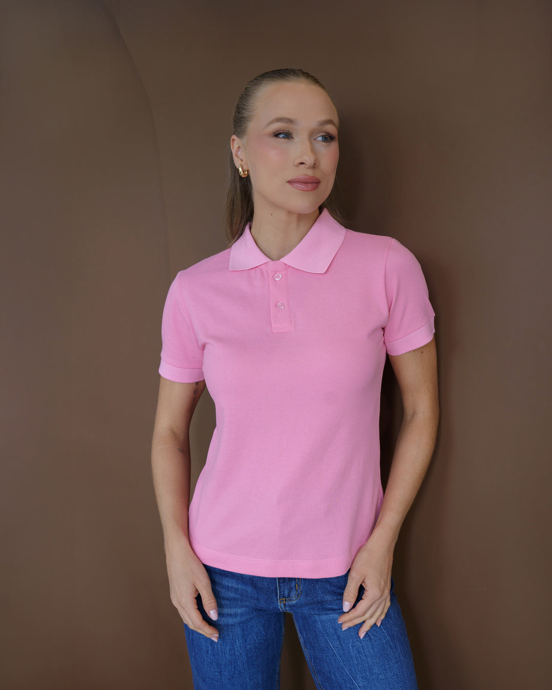 Camiseta polo feminina rosa claro em piquê, meio corpo frontal em ambiente marrom, usada com jeans — foto 2