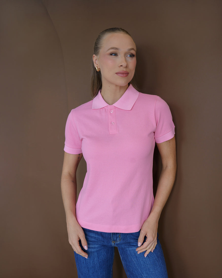 Camiseta polo feminina rosa claro em piquê, meio corpo frontal em ambiente marrom, usada com jeans