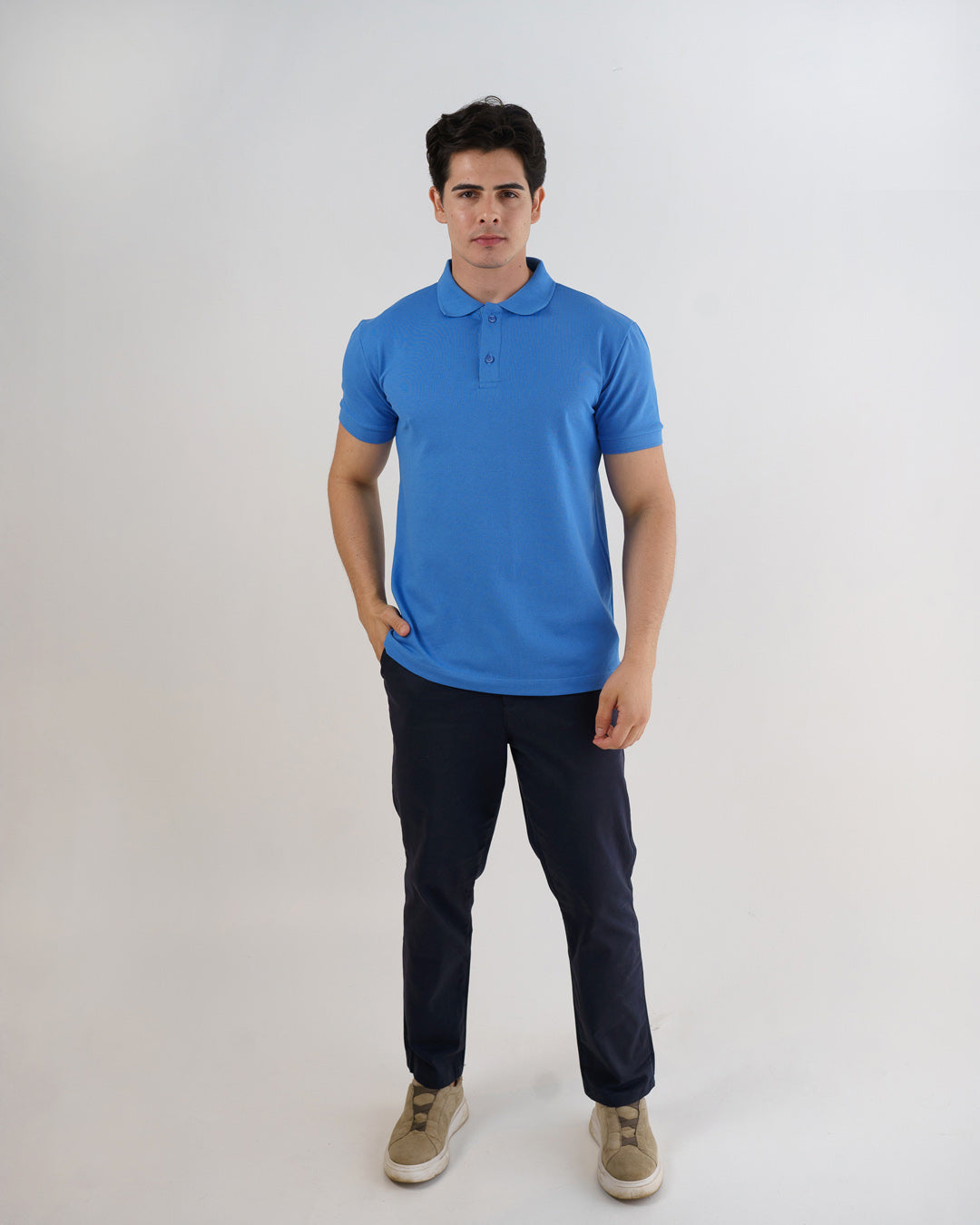 Camiseta polo masculina premium azul celeste em corpo inteiro frontal, com mão no bolso da calça — foto 5