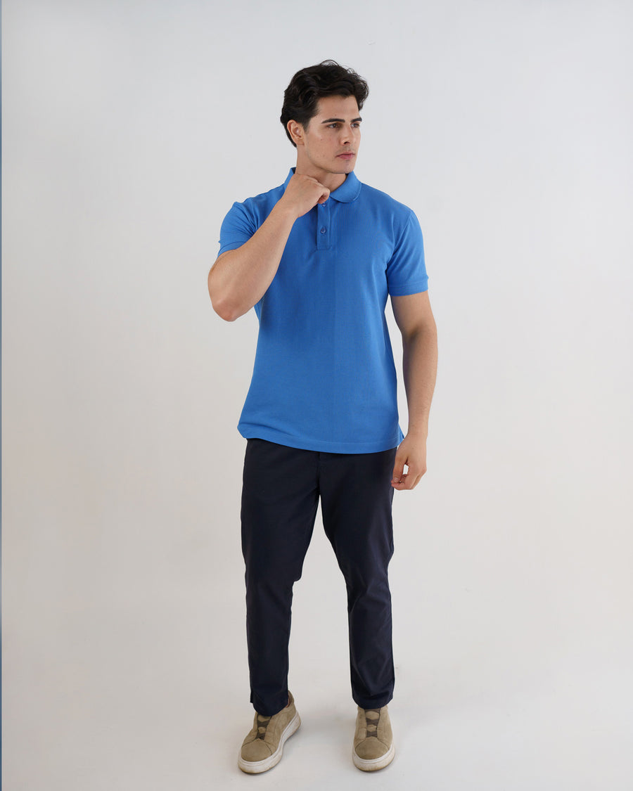 Camiseta polo masculina azul celeste em corpo inteiro, modelo ajusta a gola mostrando o caimento