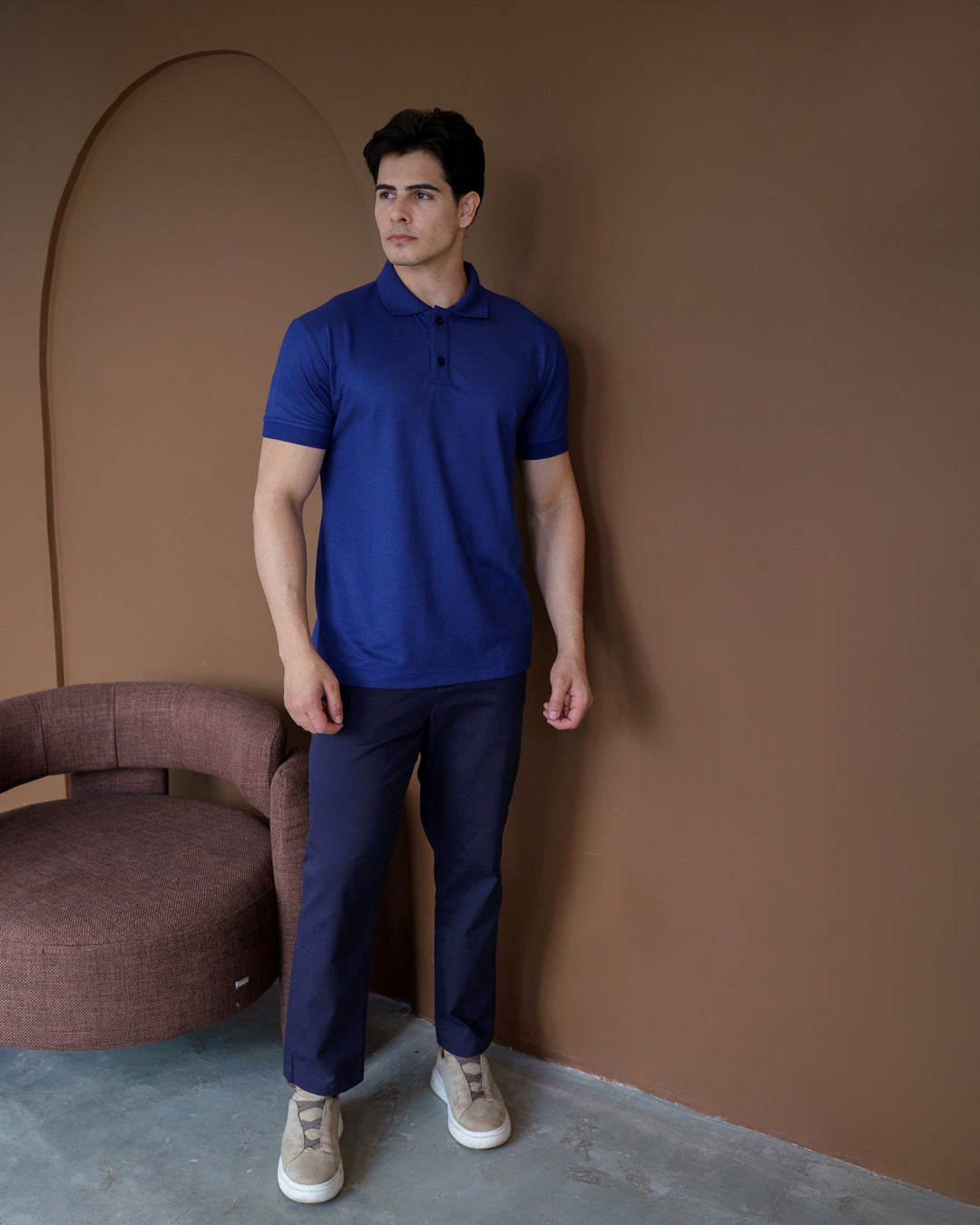 Camiseta polo masculina azul marinho em corpo inteiro, modelo veste a polo em ambiente marrom — foto 2