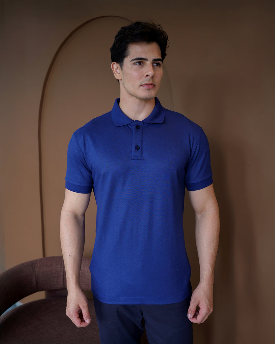 Camiseta polo masculina premium azul marinho, meio corpo frontal em ambiente marrom com poltrona
