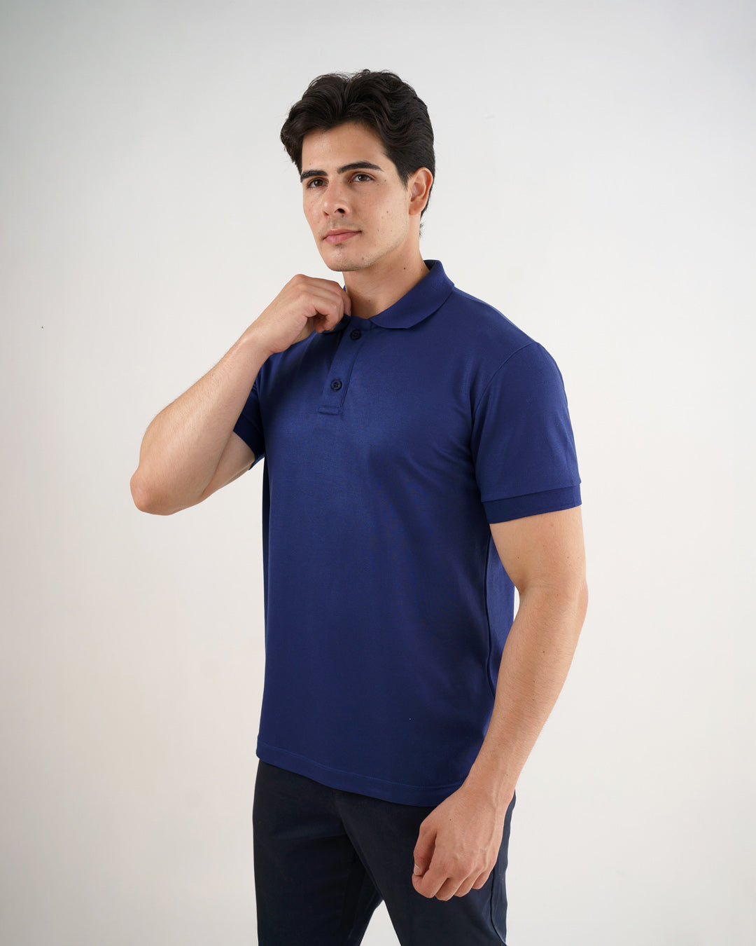 Camiseta polo masculina azul marinho em leve perfil, modelo ajusta a gola mostrando mangas com punho — foto 5