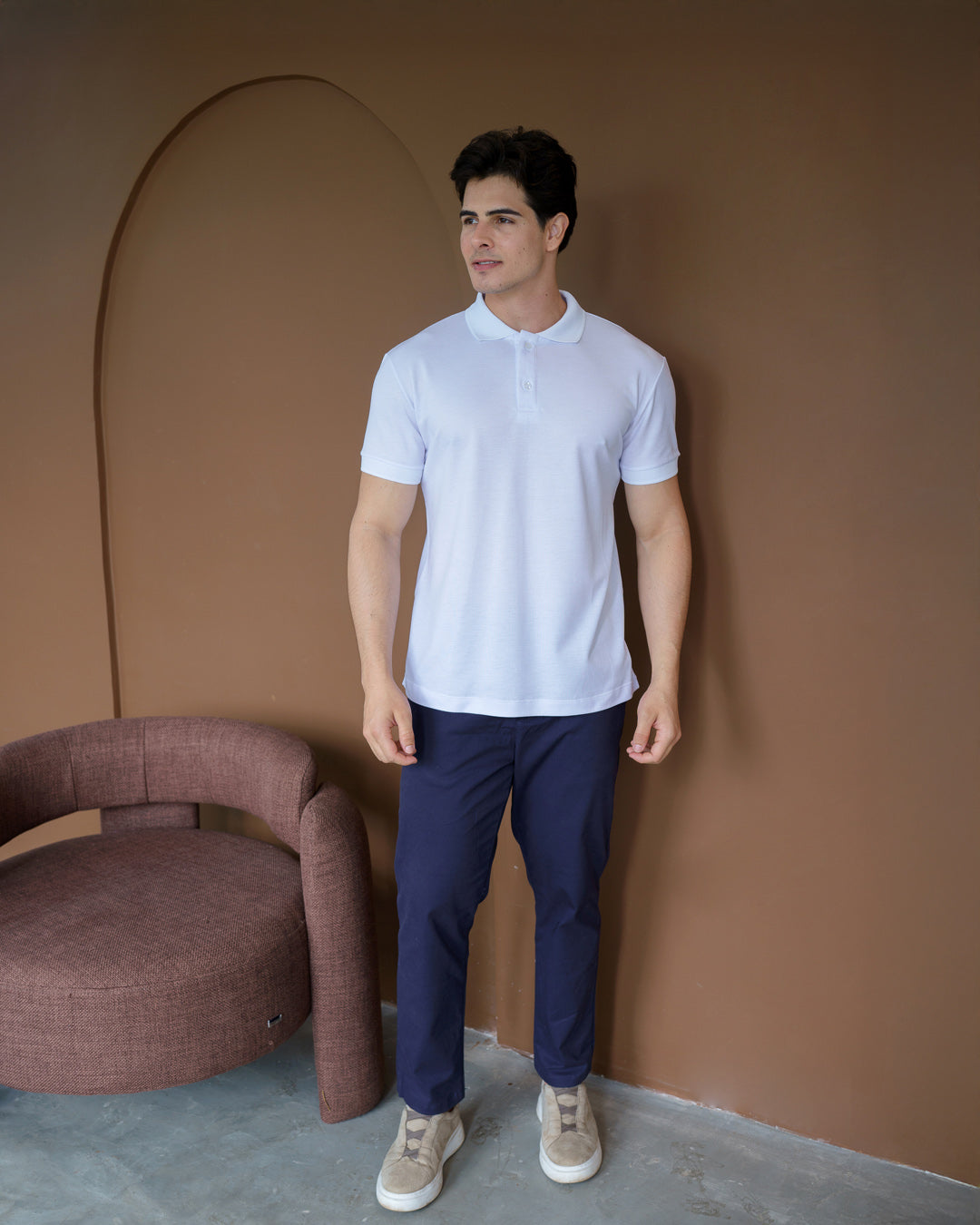 Camiseta polo masculina premium branca de corpo inteiro em cenário com poltrona, gola e botões visíveis — foto 4