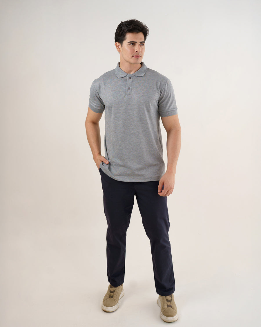 Camiseta polo masculina premium cinza claro em corpo inteiro, modelo com mão no bolso da calça azul-marinho