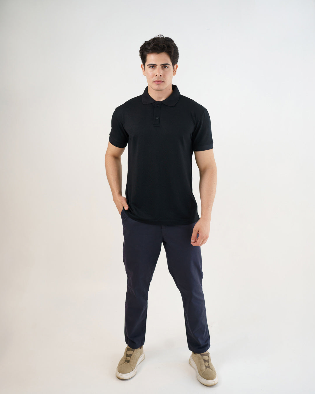 Camiseta polo masculina premium preta de frente em corpo inteiro, modelo com mão no bolso da calça azul-marinho — foto 3