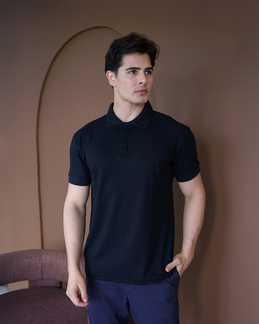 Camiseta polo masculina premium preta em meio corpo com fundo marrom, mostrando gola aberta e dois botões