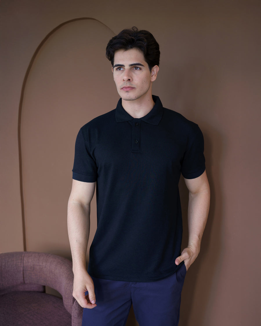 Camiseta polo masculina premium preta em ambiente interno, modelo de meio corpo com mão no bolso e gola alinhada