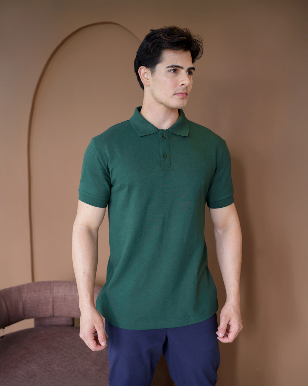 Camiseta polo masculina premium verde musgo em meio corpo com fundo marrom, gola aberta e manga curta com punho — foto 4
