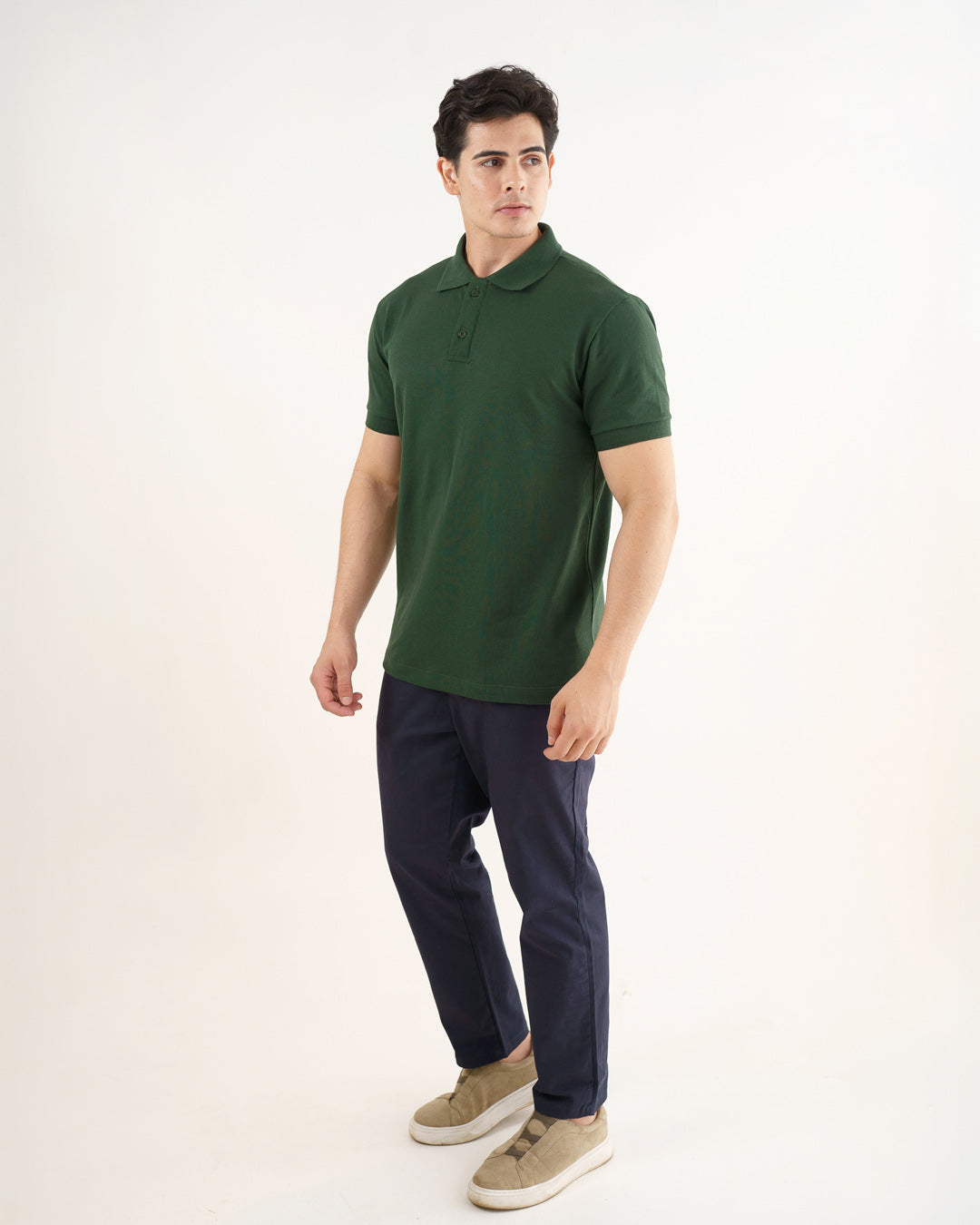 Camiseta polo masculina premium verde musgo em ângulo lateral de corpo inteiro, com calça azul-marinho e tênis — foto 5