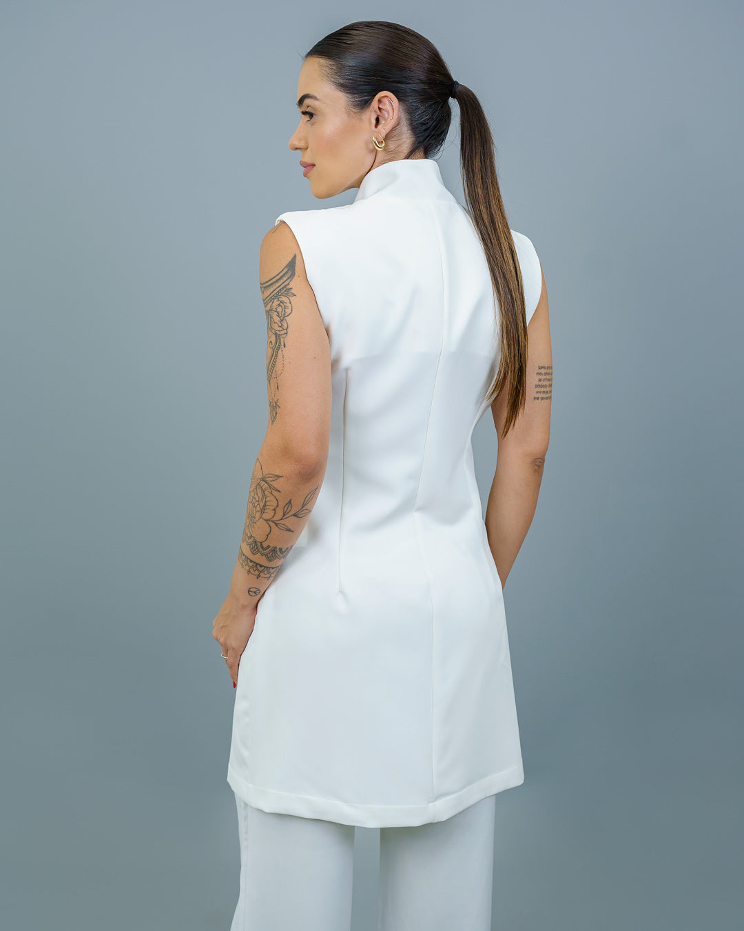 Jaleco feminino Clarice sem manga off white visto de costas na modelo, com gola alta e corte acinturado — foto 4