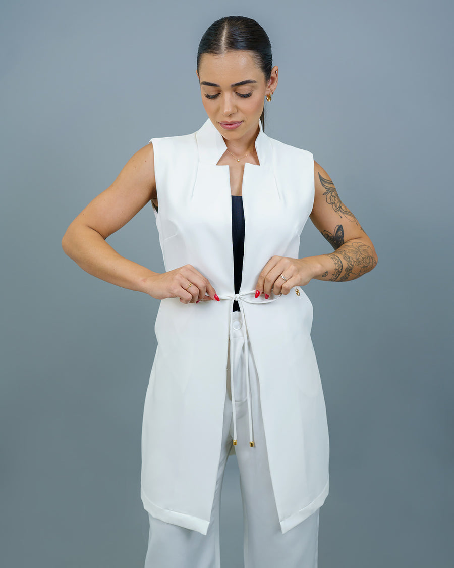 Jaleco feminino Clarice sem manga off white com modelo amarrando o laço do cordão na cintura