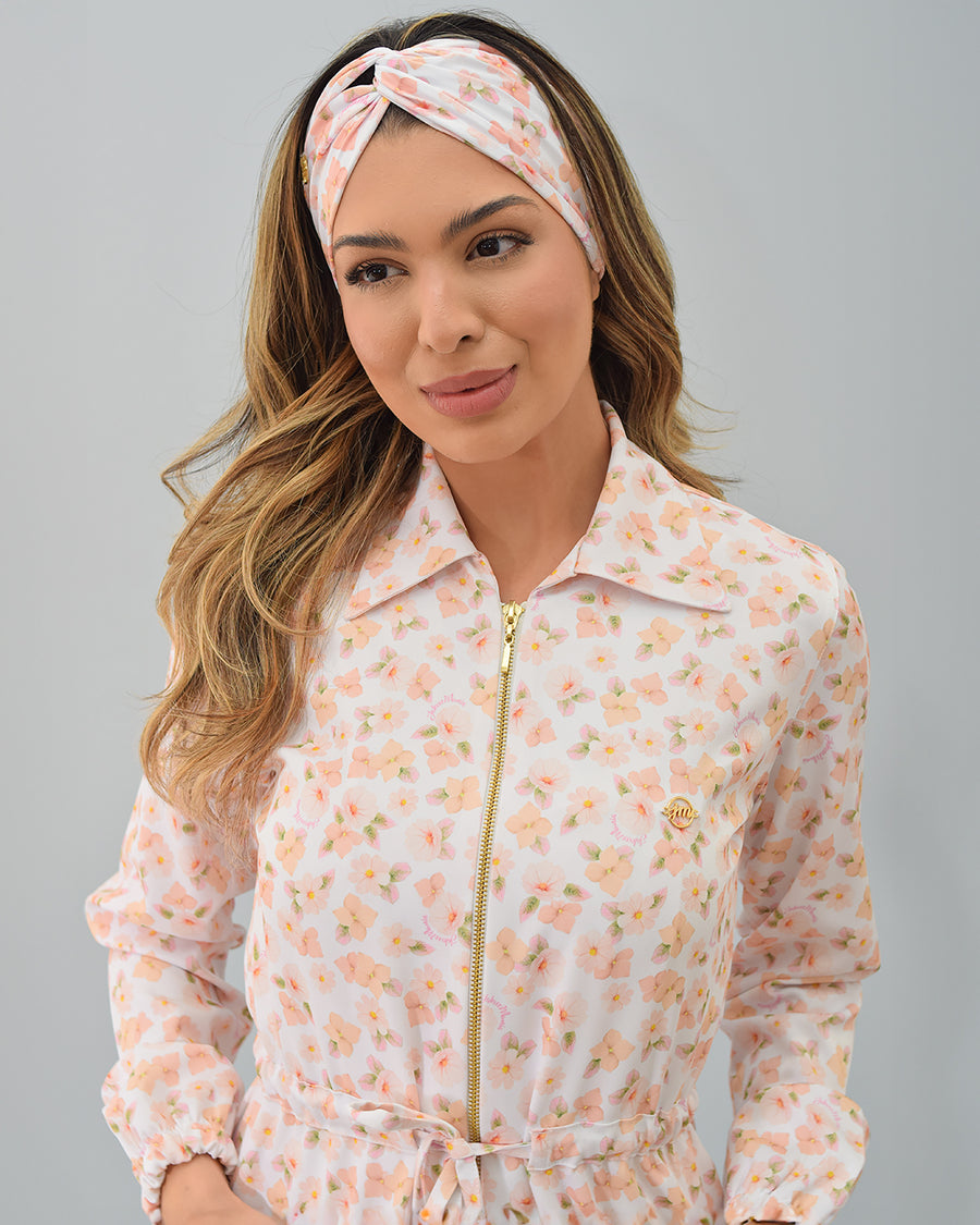 Detalhe da gola de camisa e do zíper dourado do jaleco Gardênia, com estampa floral rosê e faixa de cabelo combinando