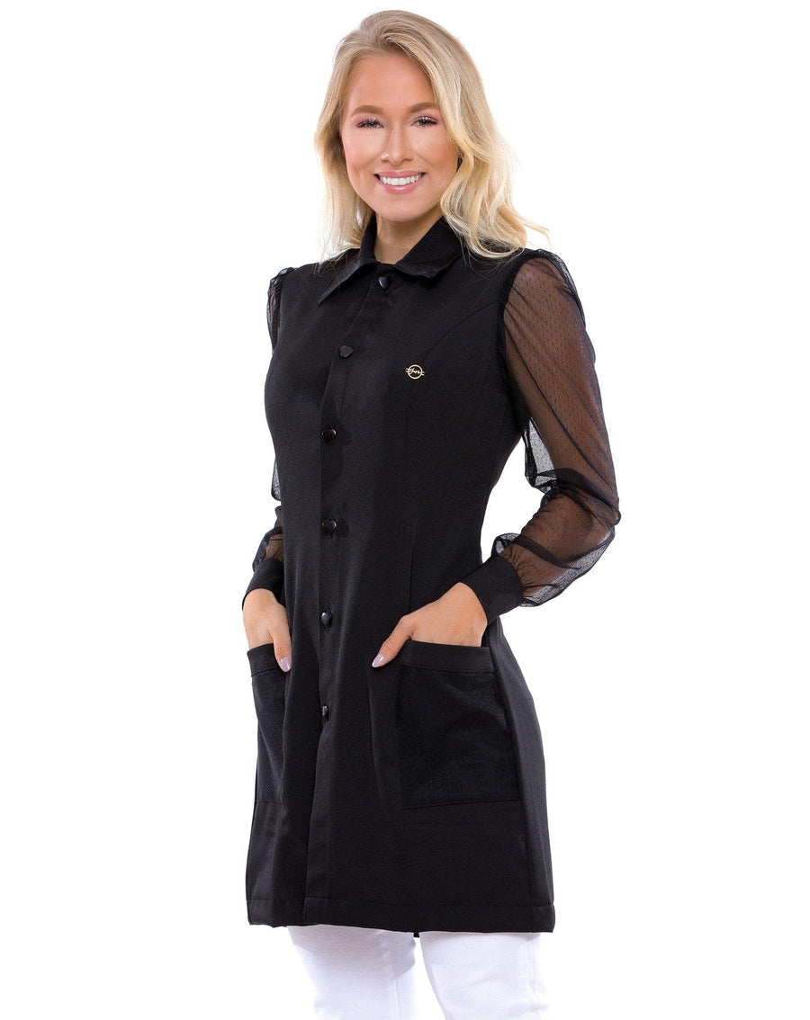 Jaleco feminino Jasmine preto em foto frontal, modelo com as mãos nos bolsos e mangas de tela transparente