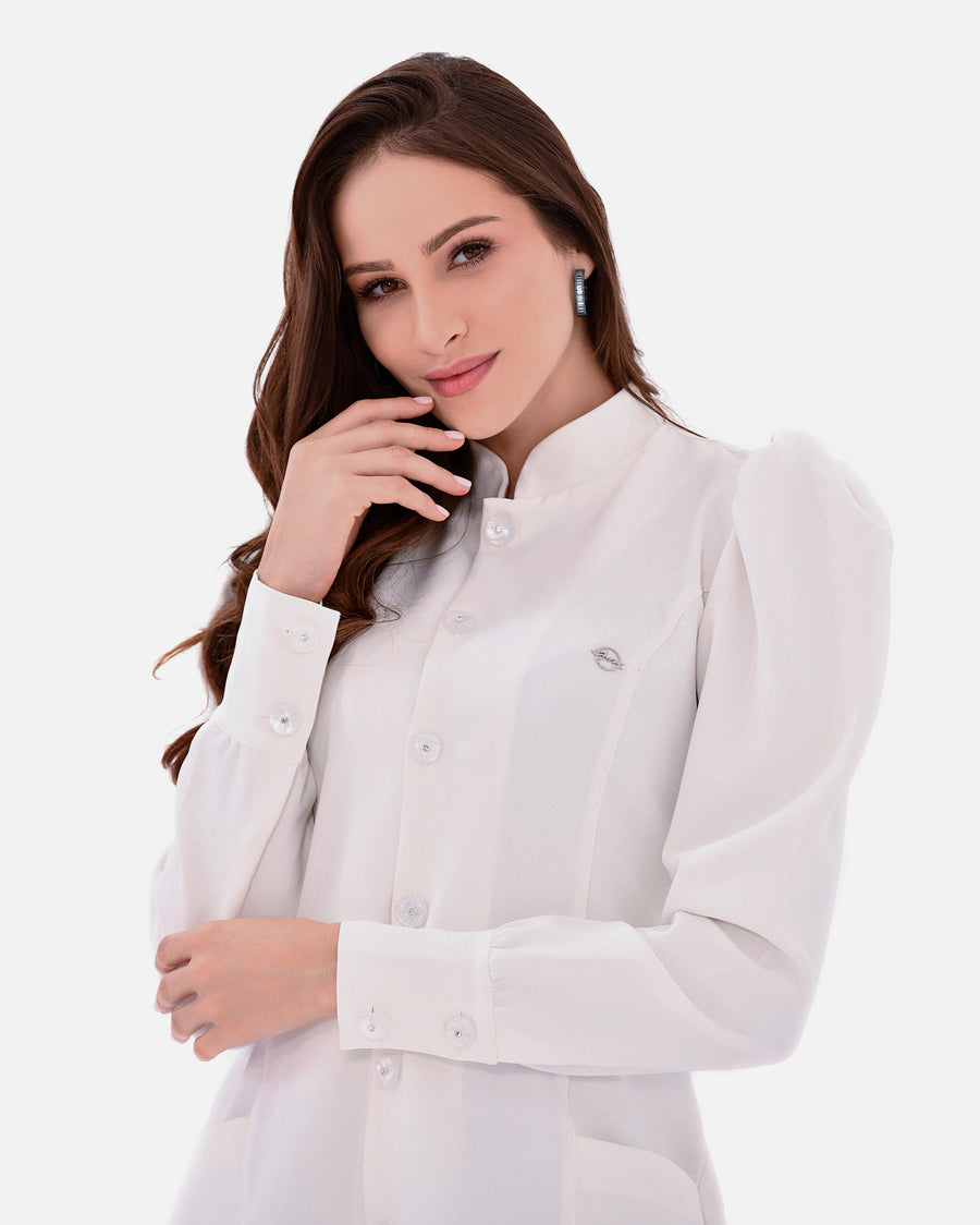 Jaleco feminino Júlia off-white em detalhe aproximado dos botões, gola padre, pin da marca e punho abotoado