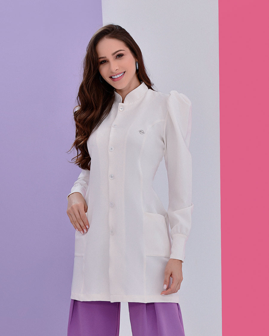 Jaleco feminino Júlia off-white em detalhe aproximado dos botões, gola padre, pin da marca e punho abotoado