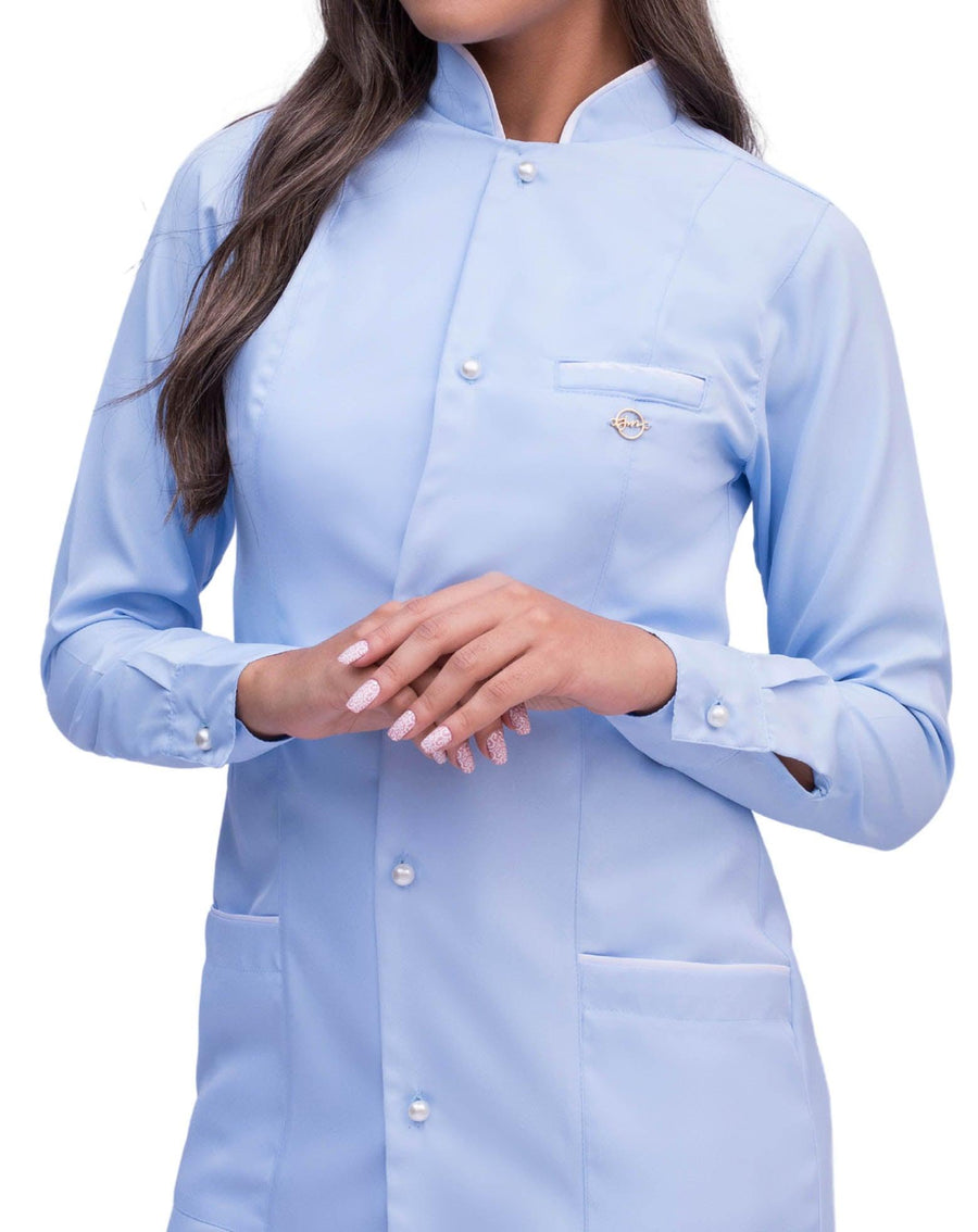 Jaleco feminino Slim Charm Color azul claro em detalhe do viés branco na gola, botões de pérola e pin dourado
