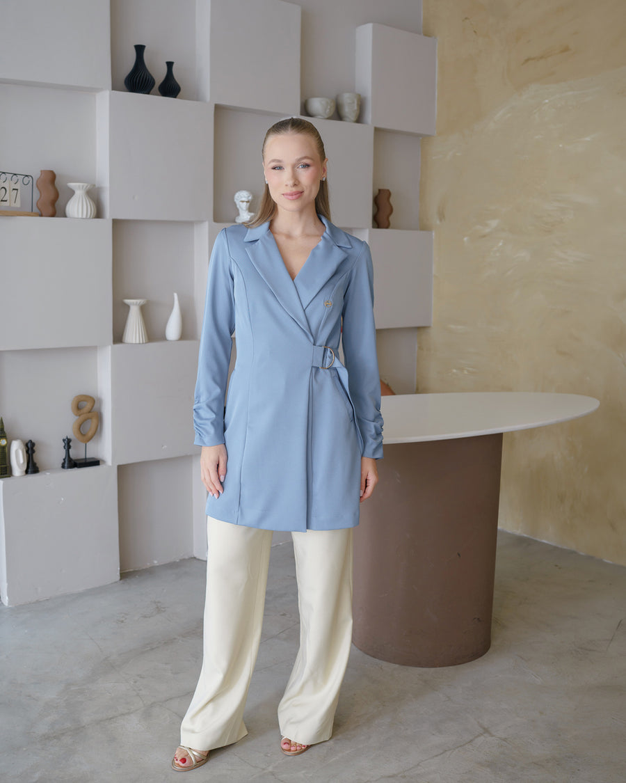 Jaleco feminino Sofia azul grafite de corpo inteiro em ambiente clean, gola de blazer e fechamento com fivela