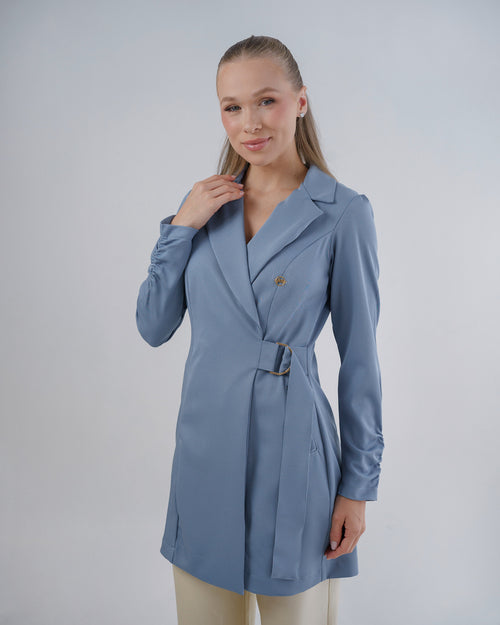 Jaleco feminino Sofia azul grafite, vista frontal em modelo, gola de blazer transpassada e fivela dourada na cintura