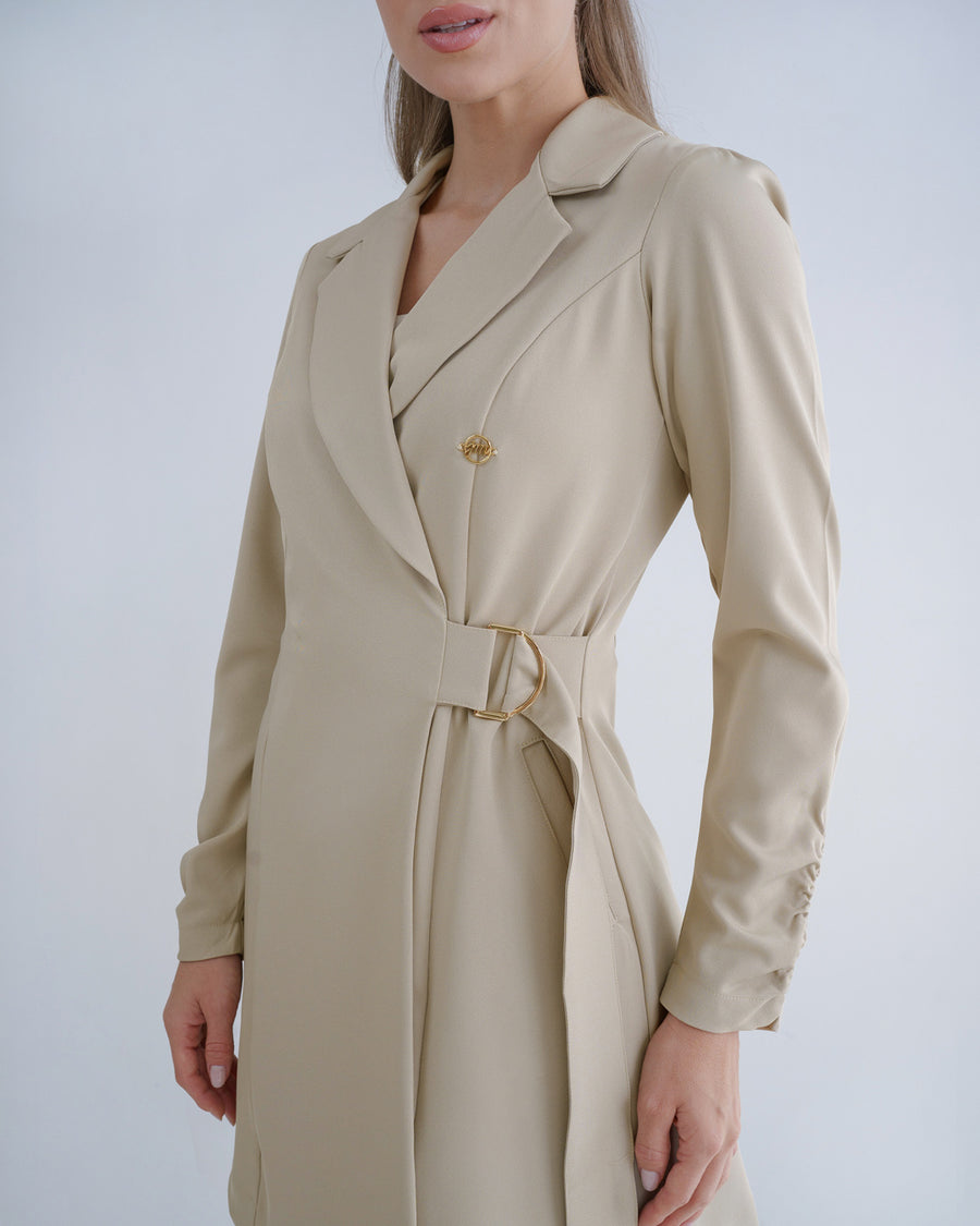 Jaleco feminino Sofia bege em close, detalhe da gola de blazer, pin dourado e fivela metálica regulável na cintura