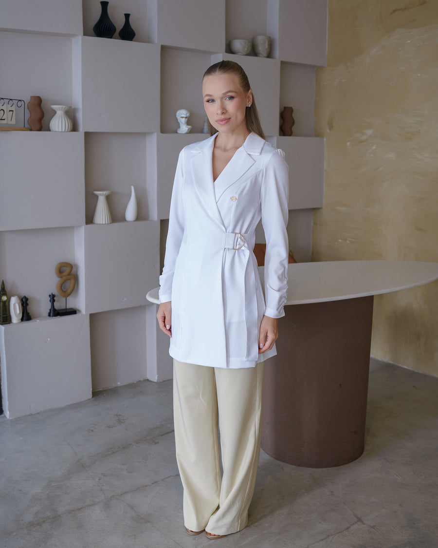 Jaleco feminino Sofia branco de corpo inteiro em ambiente clean, gola de blazer e fivela lateral na cintura