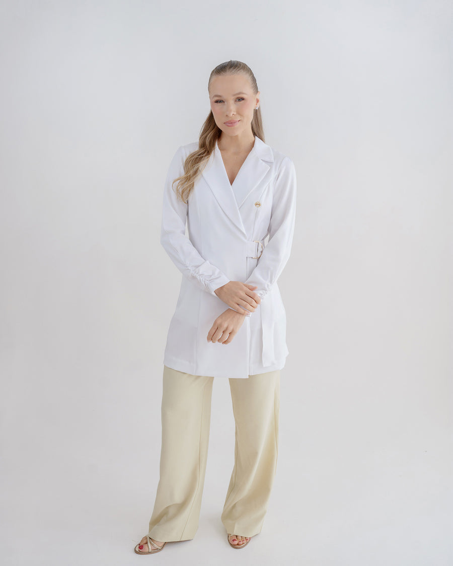 Jaleco feminino Sofia branco de corpo inteiro em fundo neutro, frente transpassada com faixa e botão dourado