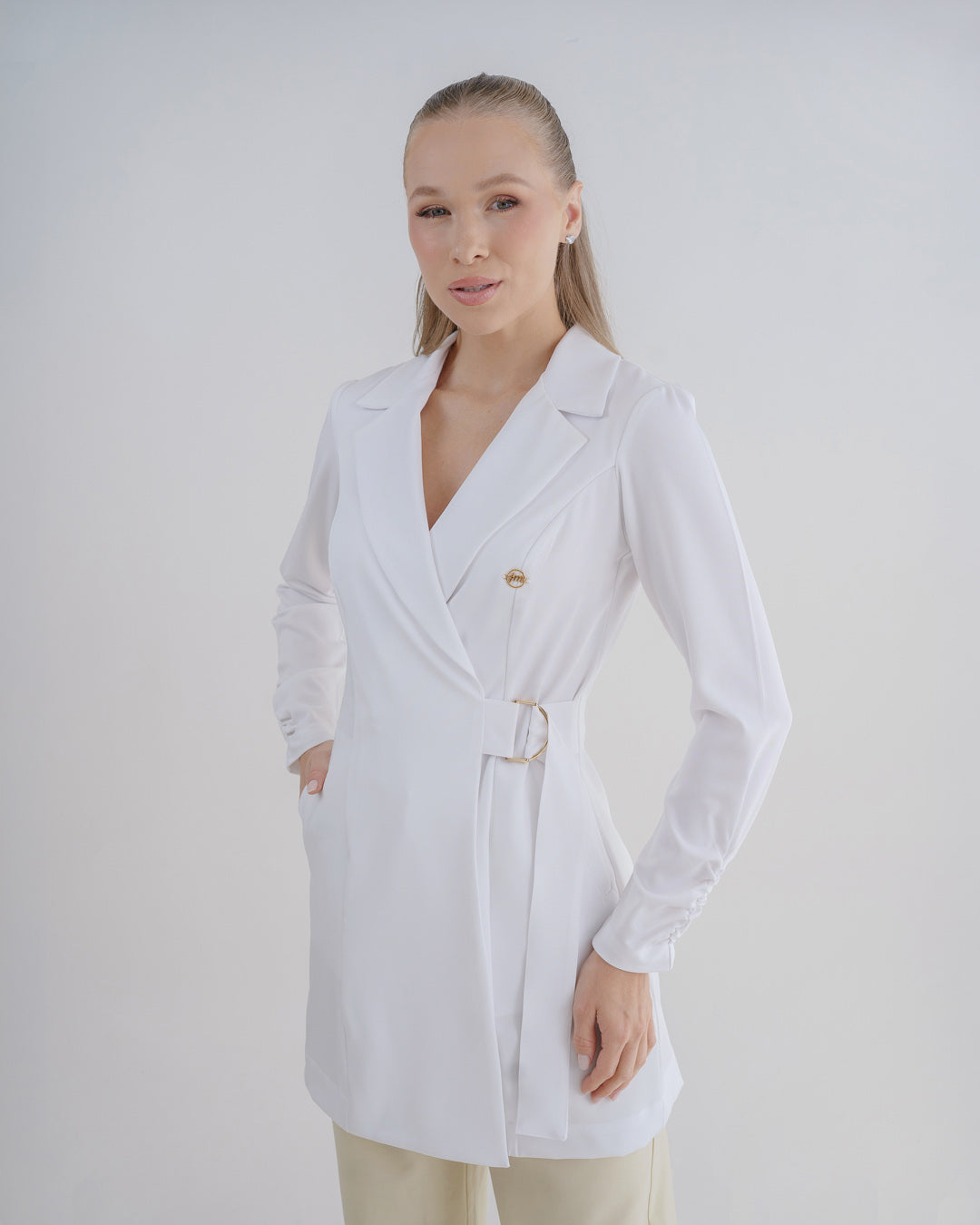 Jaleco feminino Sofia branco, vista frontal em modelo, gola de blazer transpassada e fivela dourada na cintura