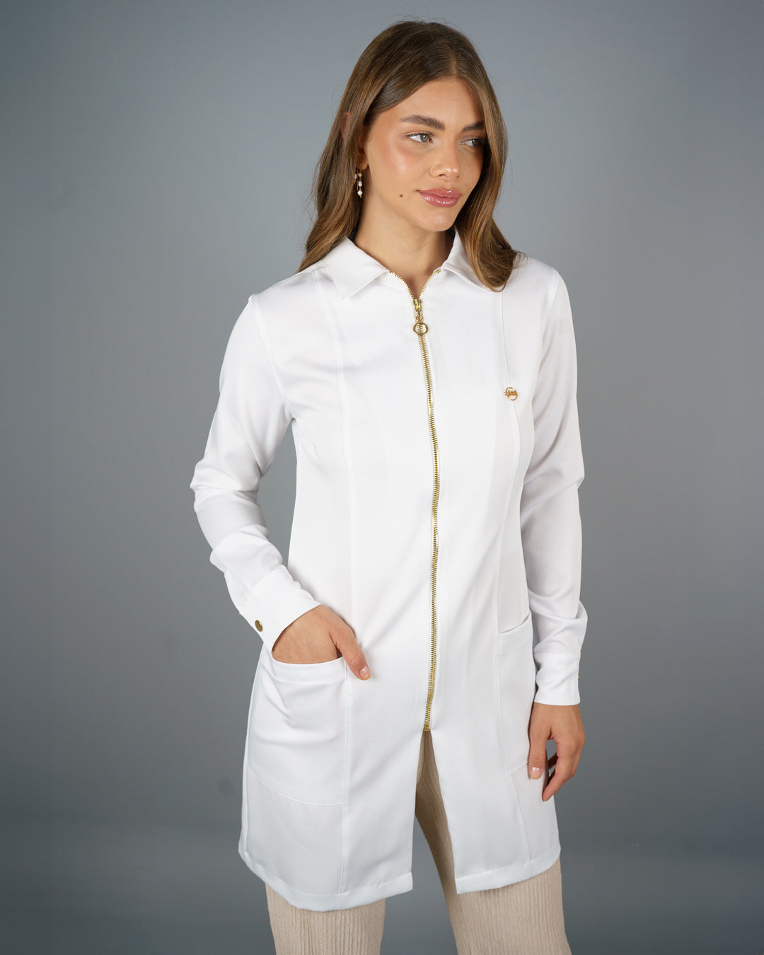 Jaleco feminino Valentine branco em meio corpo, mão no bolso frontal, zíper dourado e pin dourado no peito — foto 4
