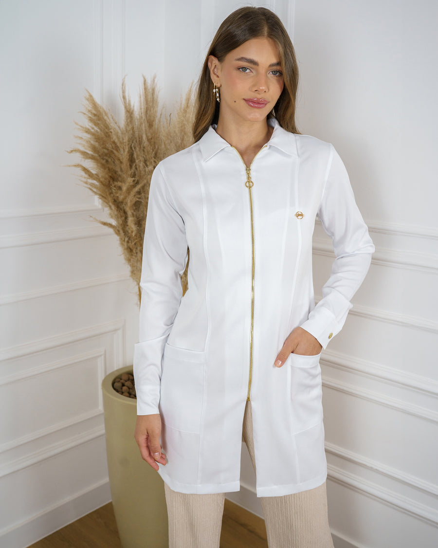 Jaleco feminino Valentine branco em meio corpo, modelo com mão no bolso, gola esporte e zíper dourado frontal