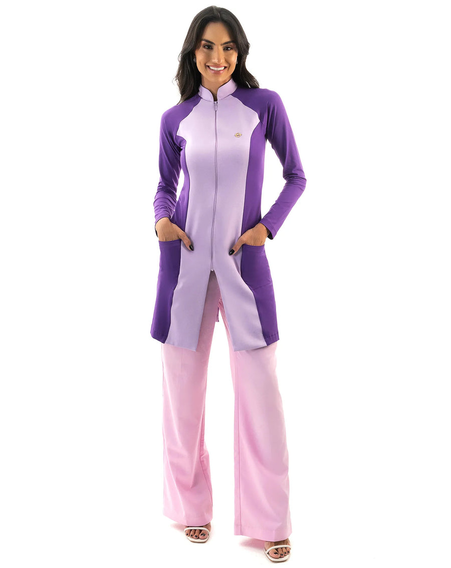 Jaleco feminino Vicky lavanda com roxo de corpo inteiro, modelo de frente com as mãos nos bolsos roxos