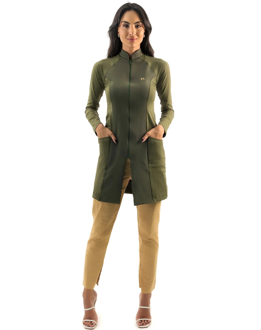 Jaleco feminino Vicky verde militar de corpo inteiro, modelo de frente com as mãos nos bolsos e calça caramelo