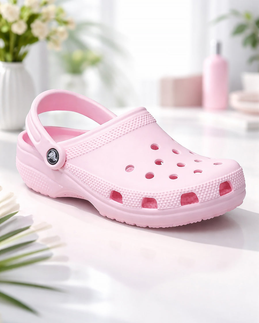 Sandália Crocs Classic Clog Pink Milk rosa claro em close sobre mesa clara com flores ao fundo e furos em destaque