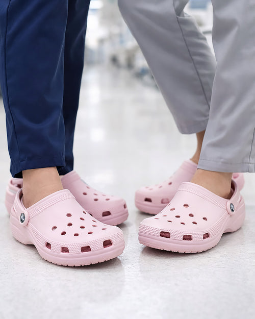 Sandália Crocs Classic Clog Pink Milk rosa claro em uso nos pés de duas pessoas em ambiente de piso claro
