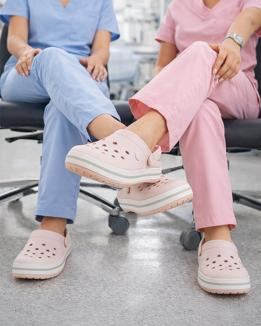 Sandália Crocs Crocband Clog Quartz nos pés de duas profissionais sentadas, destaque para o solado com faixa branca
