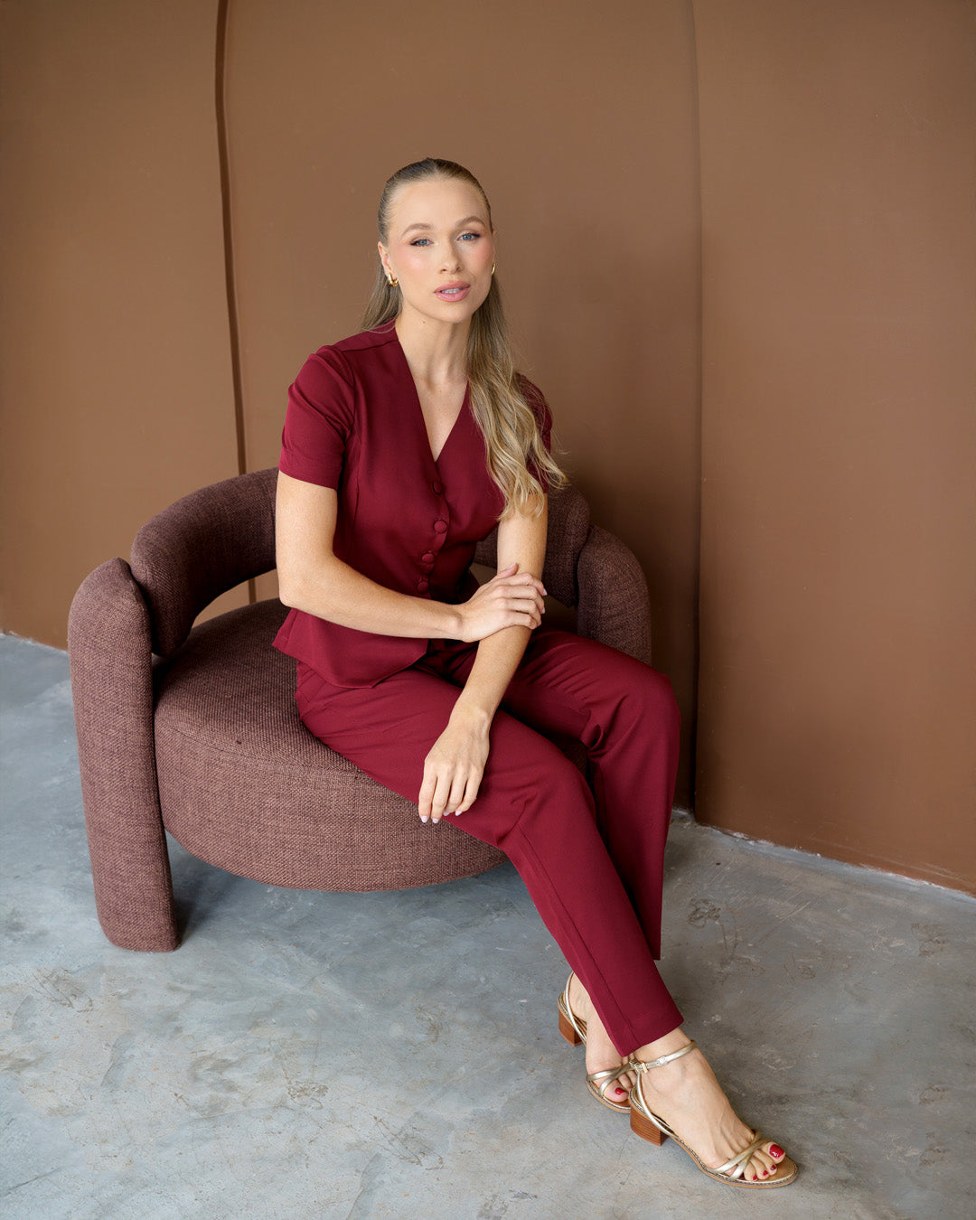 Scrub feminino Classic bordô em modelo sentada, mostrando o caimento da blusa com botões e da calça — foto 3