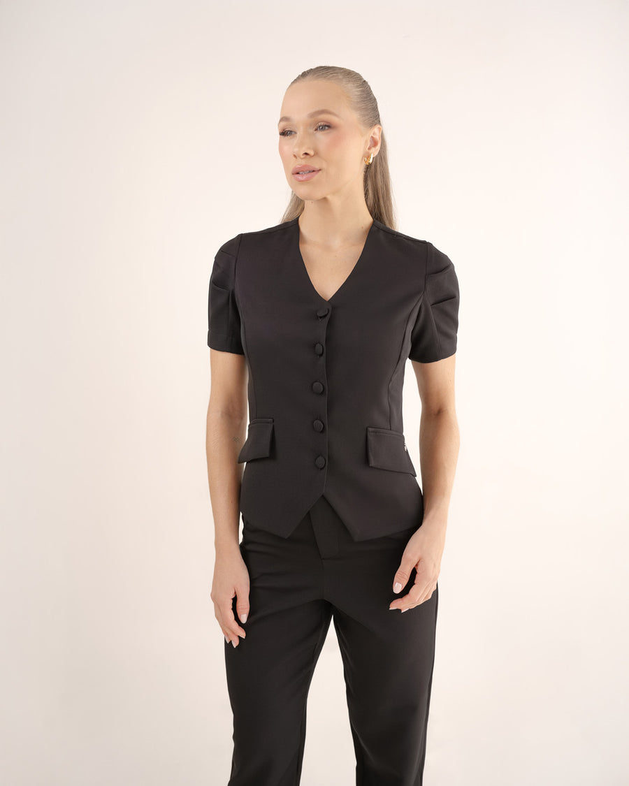 Scrub feminino Classic preto de frente em meio corpo, gola V, botões forrados e bolsos com lapela