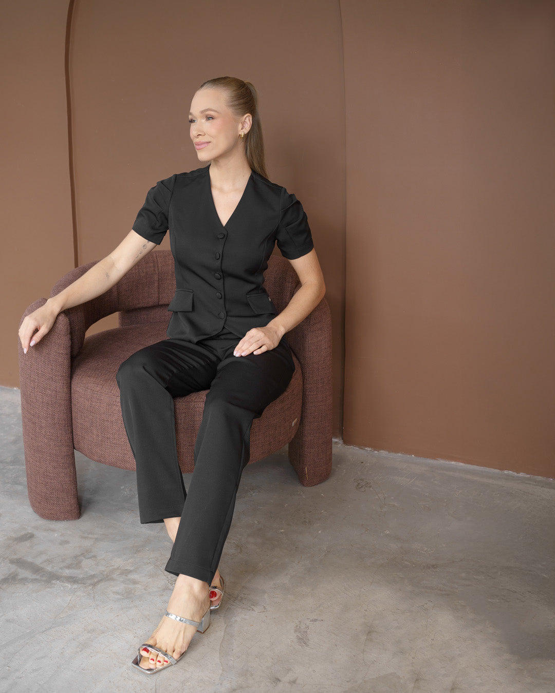Scrub feminino Classic preto em modelo sentada, mostrando o caimento da blusa com botões e da calça — foto 4