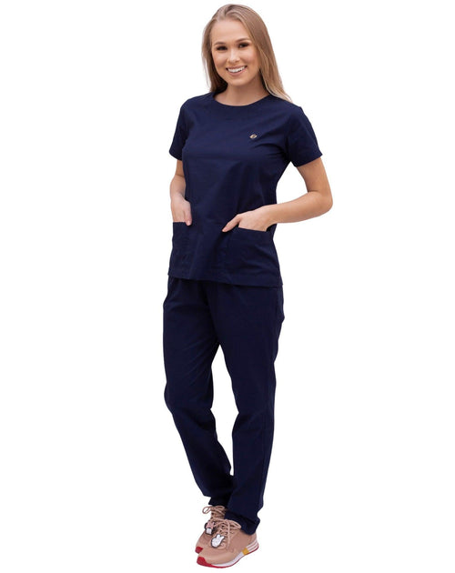 Scrub feminino Confort azul marinho em corpo inteiro, modelo com as mãos nos bolsos frontais da blusa