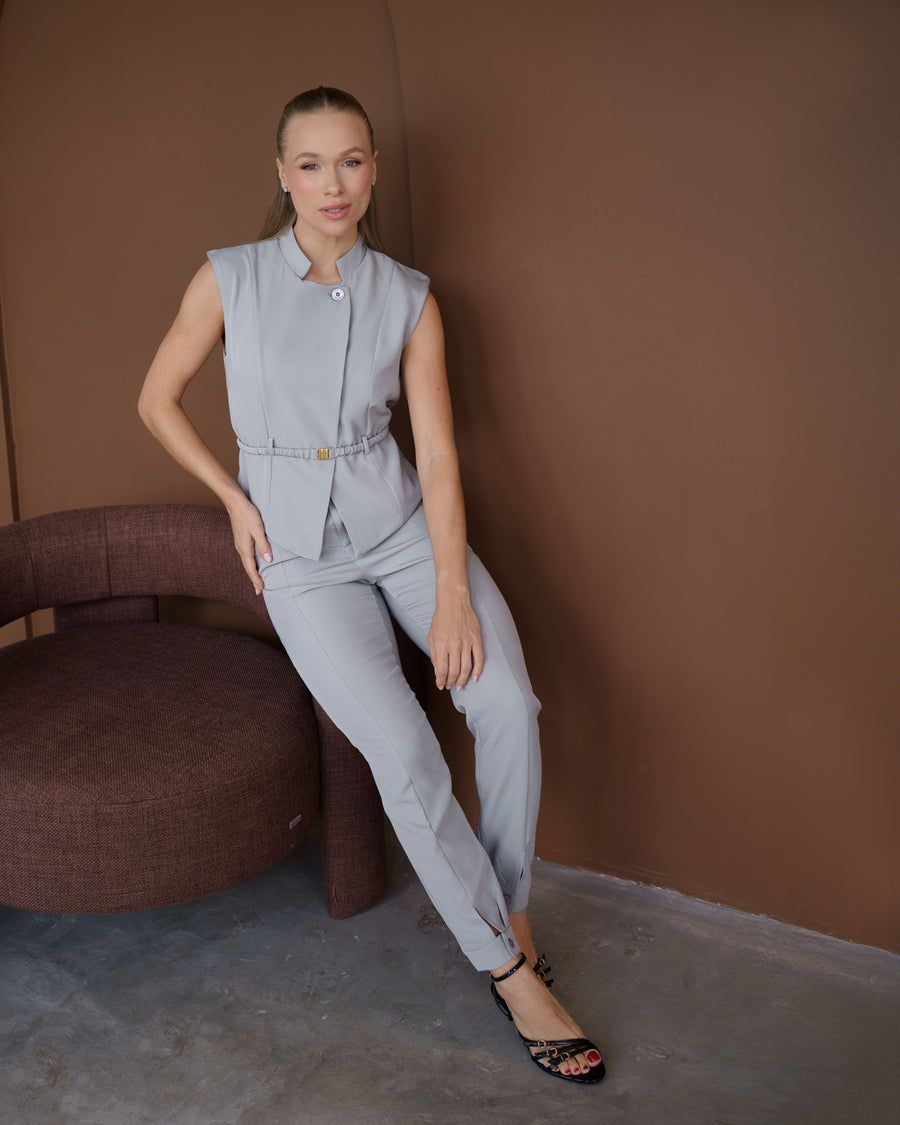 Scrub feminino Ella cinza claro, modelo apoiada em poltrona mostrando o conjunto de blusa com cinto e calça slim